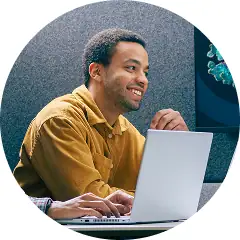 Young man working on a laptop in a modern biotech lab setting.